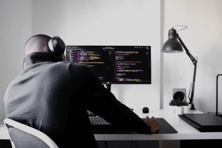 homem preocupado sentado na cadeira de frente para um computador com códigos na tela