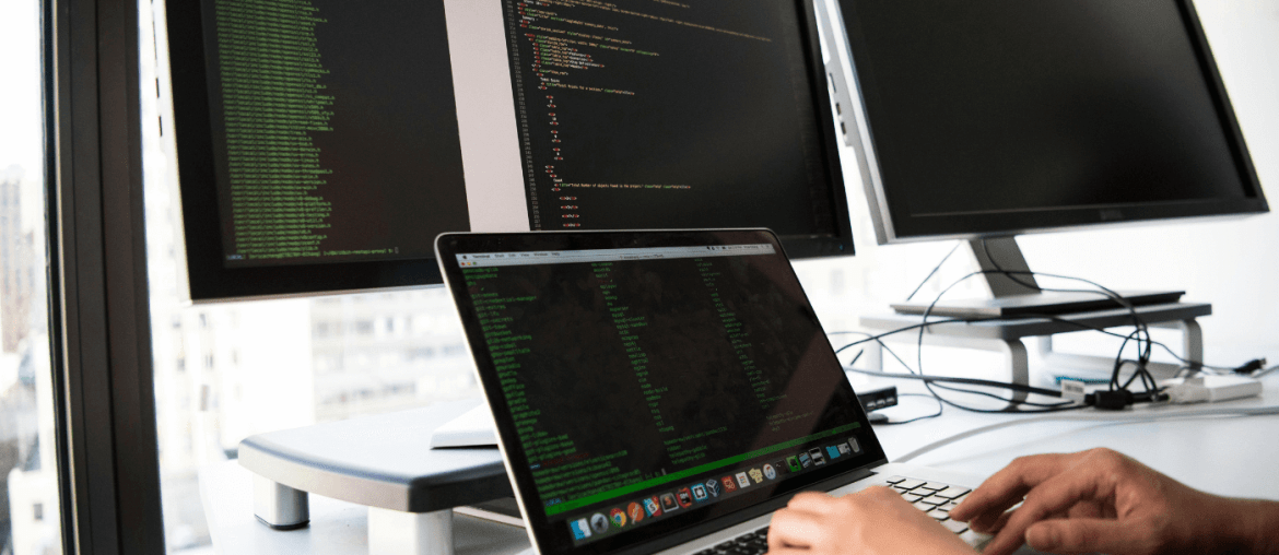 Capa do artigo com uma pessoa utilizando notebook sobre a mesa com vários monitores