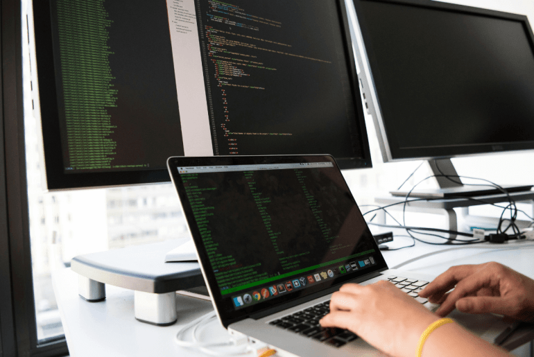 Capa do artigo com uma pessoa utilizando notebook sobre a mesa com vários monitores